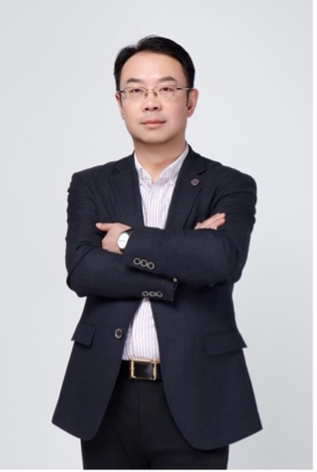 Charles is wearing a dark jacket and white shirt. He is standing with his arms folded and looking at the camera.